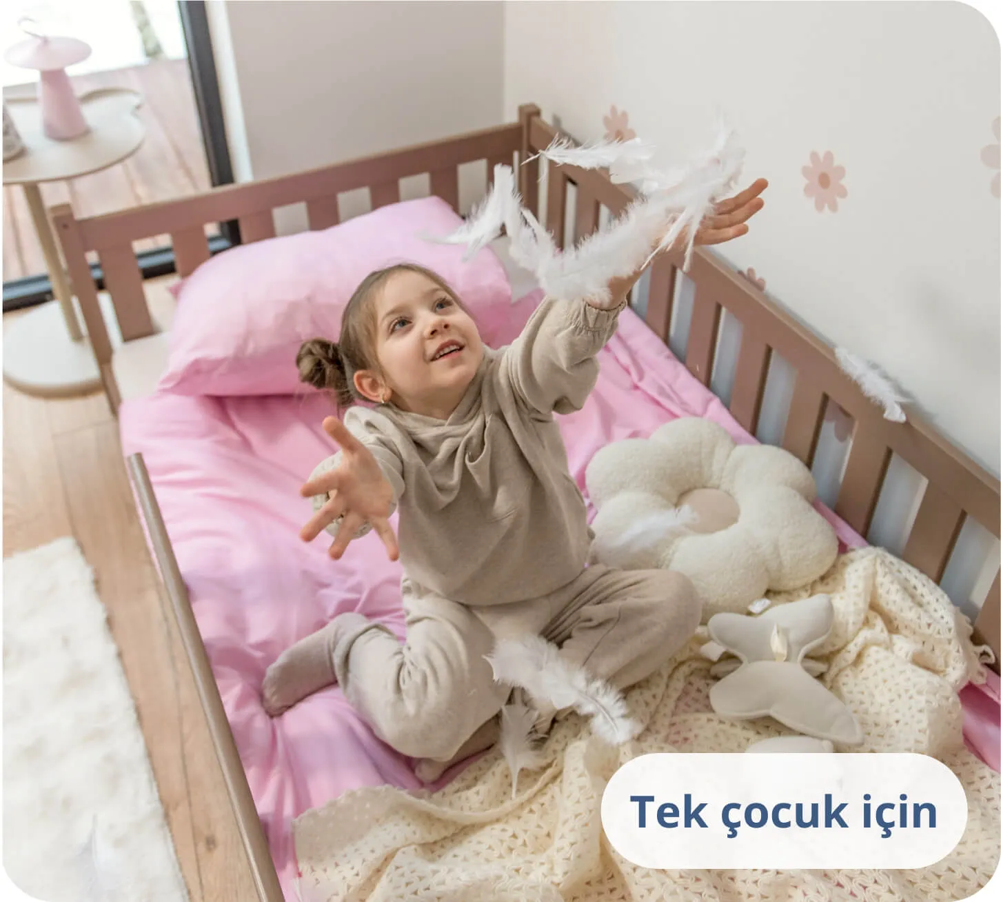 Çikolata renkli bir yatakta, pembe nevresimler üzerinde beyaz tüylerle oynayan kız çocuğu.